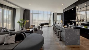 A modern living room with a large sofa, a piano, and a bar area with stools. - The Joseph, a Luxury Collection Hotel, Nashville (Nashville)