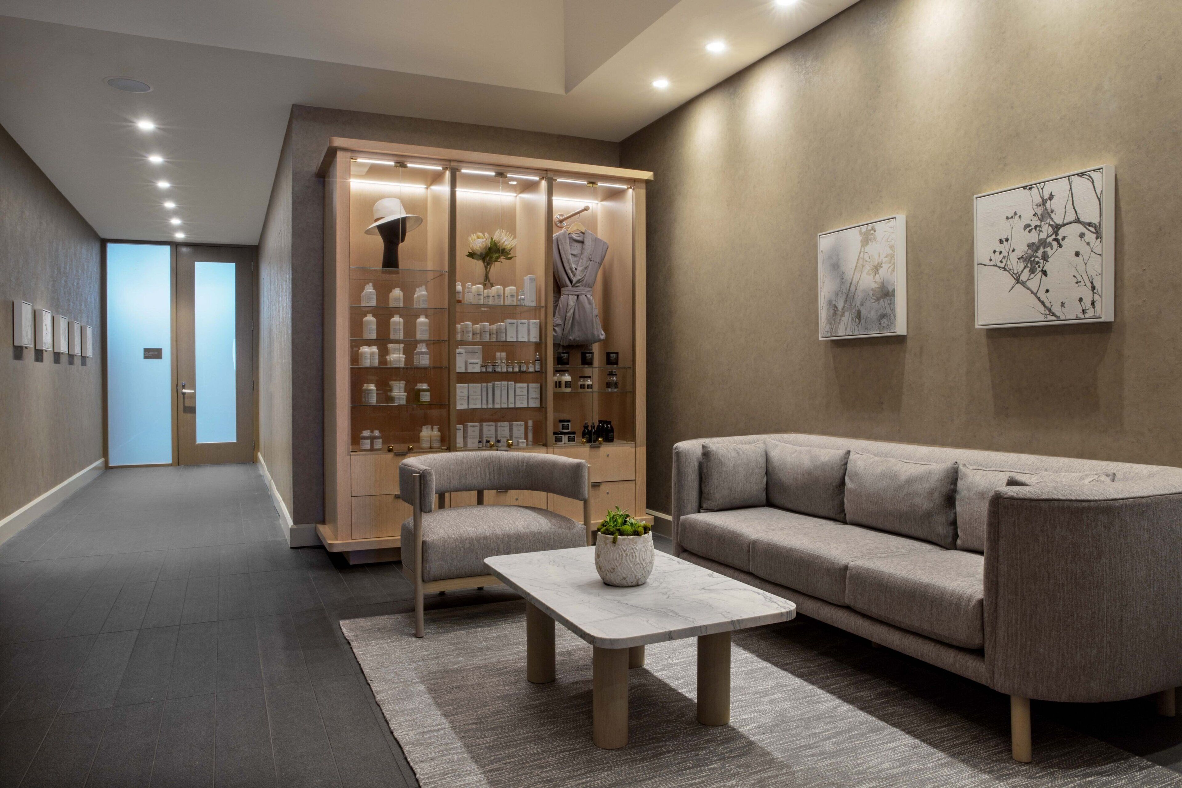 A modern lobby with a sofa, chairs, a coffee table, a reception desk, and a display of toiletries.
