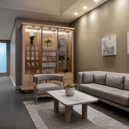 A modern lobby with a sofa, chairs, a coffee table, a reception desk, and a display of toiletries.