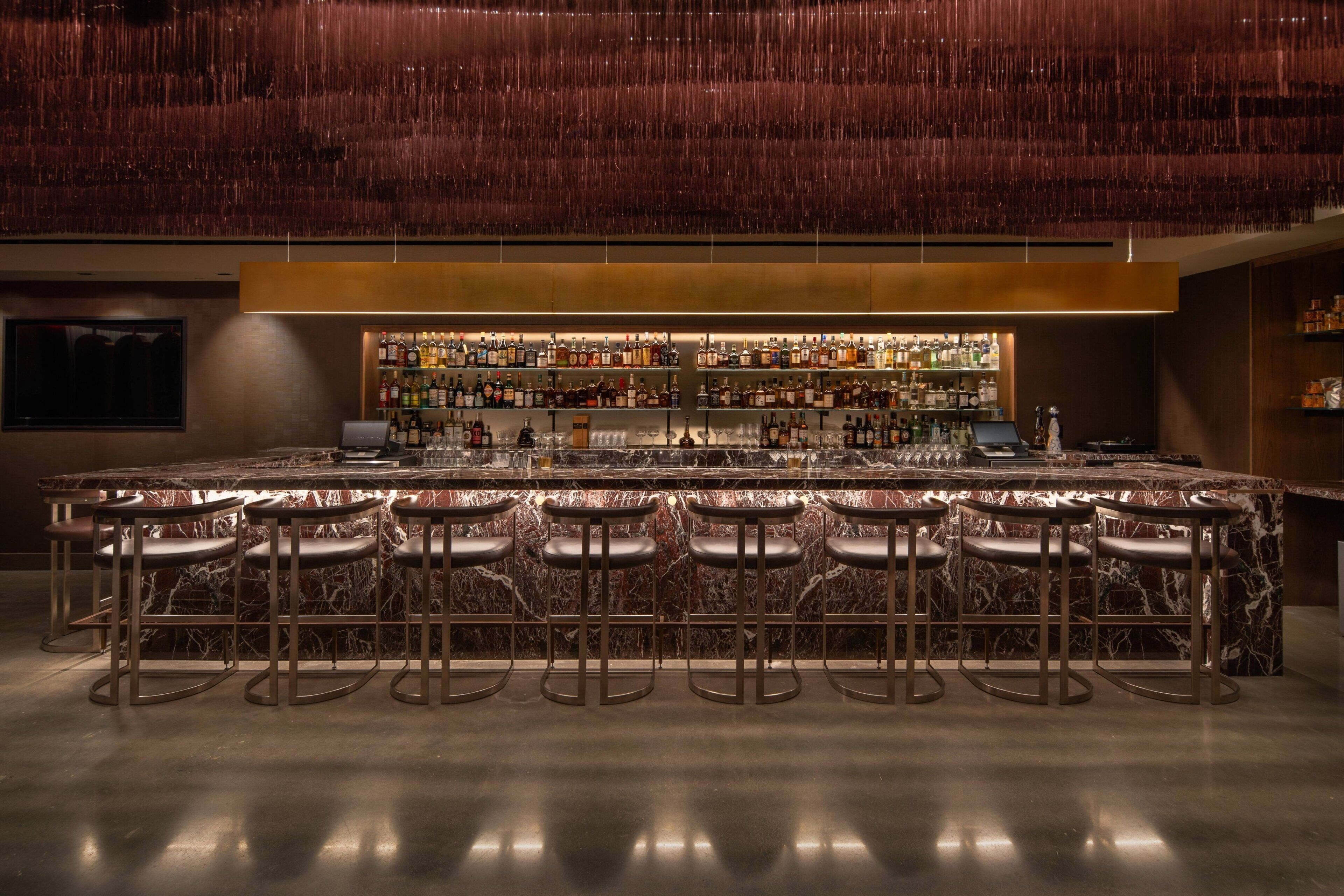 A bar area with a marble countertop, multiple stools, and a well-stocked bar.