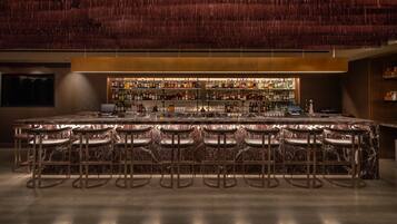 A bar area with a marble countertop, multiple stools, and a well-stocked bar.