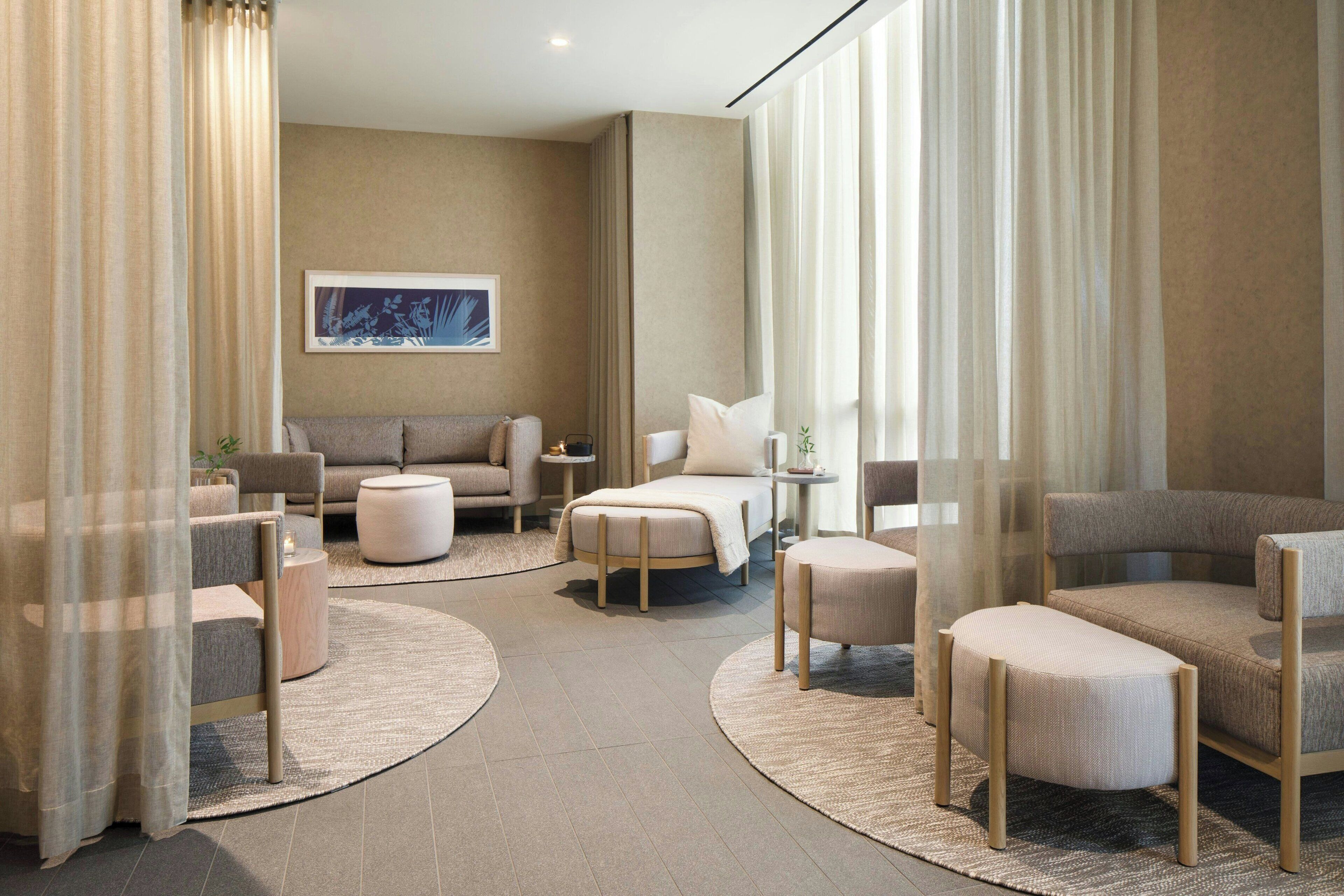 Een moderne hotelkamer met een bank, twee fauteuils, een bijzettafeltje, een bed en een klein nachtkastje.