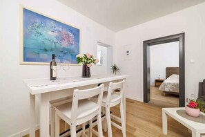 A room with a white desk, chairs, a painting, a bed, and a small table with flowers.
