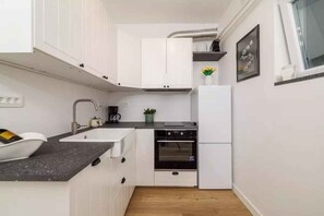 A compact kitchen with white cabinetry, a black oven, a sink, and a countertop.