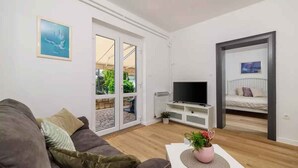 Uma sala de estar moderna com sofá, televisão de tela plana, mesa de centro com planta e porta de vidro deslizante que dá para área externa.