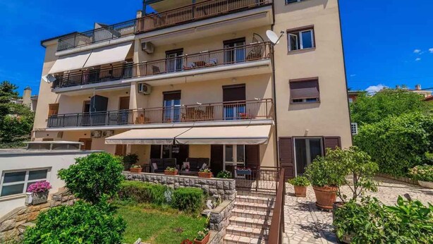 Um edifício residencial com vários andares, varandas, área de estar coberta ao ar livre e um jardim.