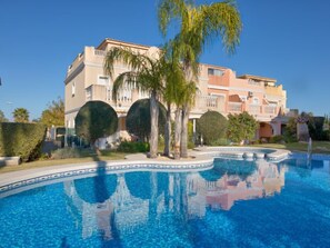 Ein Hotel mit Swimmingpool, Palmen und einem Gebäude im mediterranen Stil.