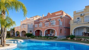Una grande piscina con un elemento d'acqua cristallina circondata da un giardino curato e un edificio a più piani con balconi.