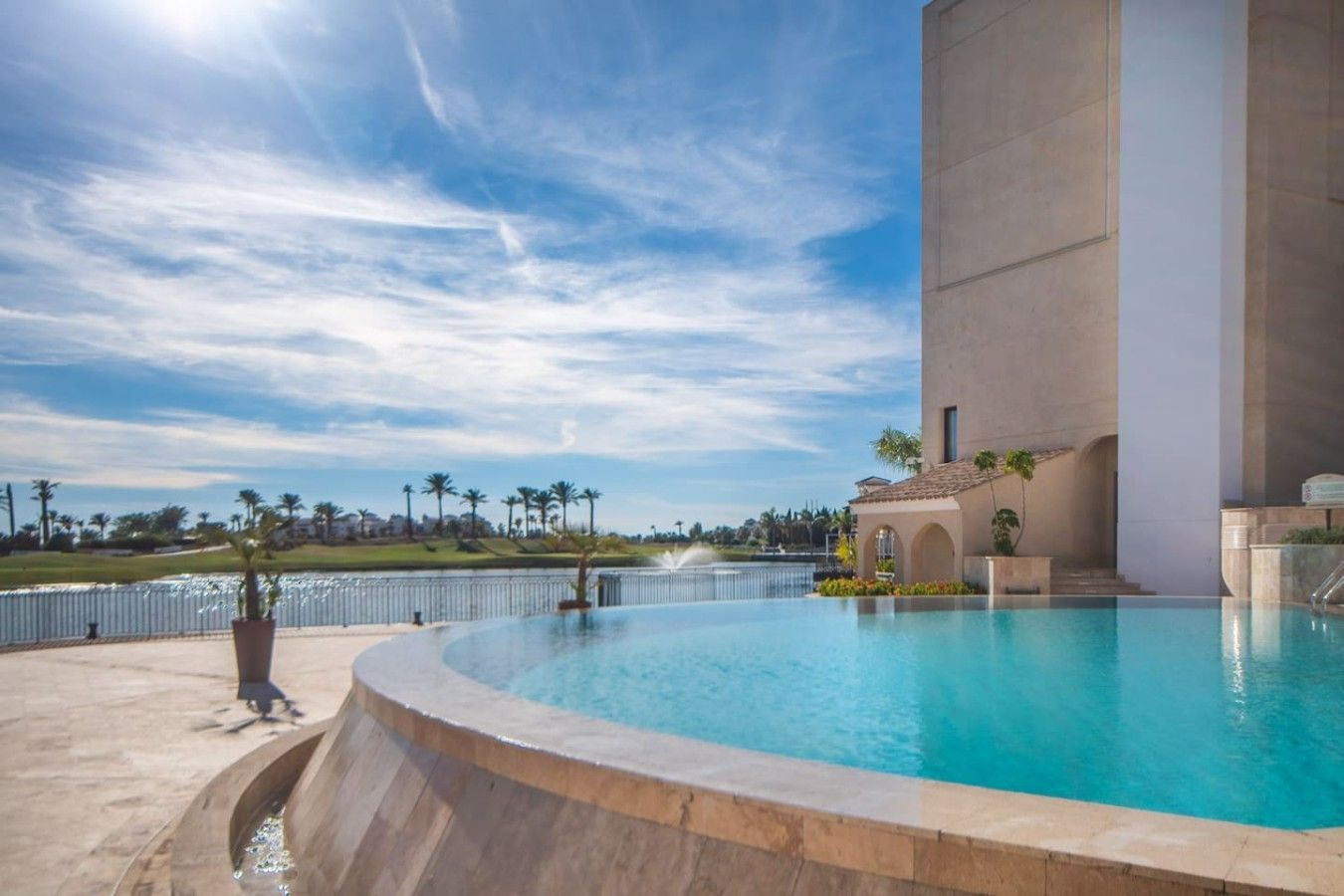A swimming pool with a curved edge, a large building with a flat roof, and a clear sky.