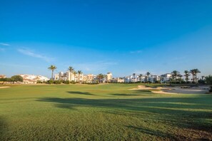 A golf course with a clear sky, palm trees, and buildings in the background. - Bright 2 Bedroom Villa with Private Pool - LO4LT (Torre-Pacheco)