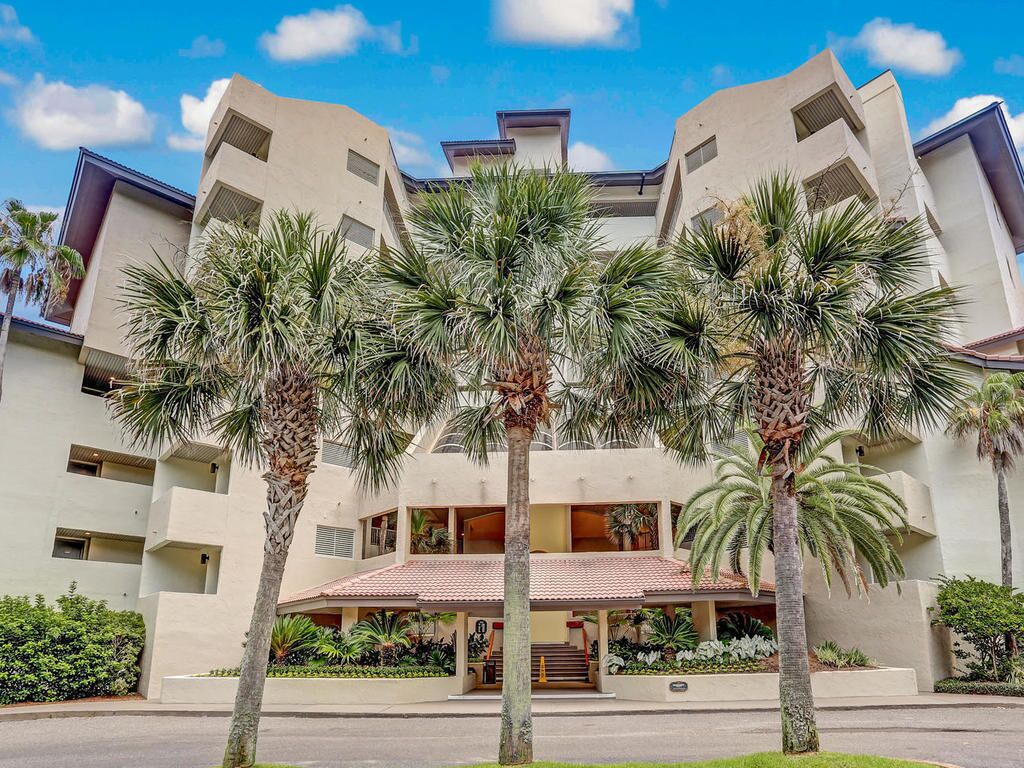 A modern hotel with a symmetrical facade, multiple balconies, and palm trees in the foreground.