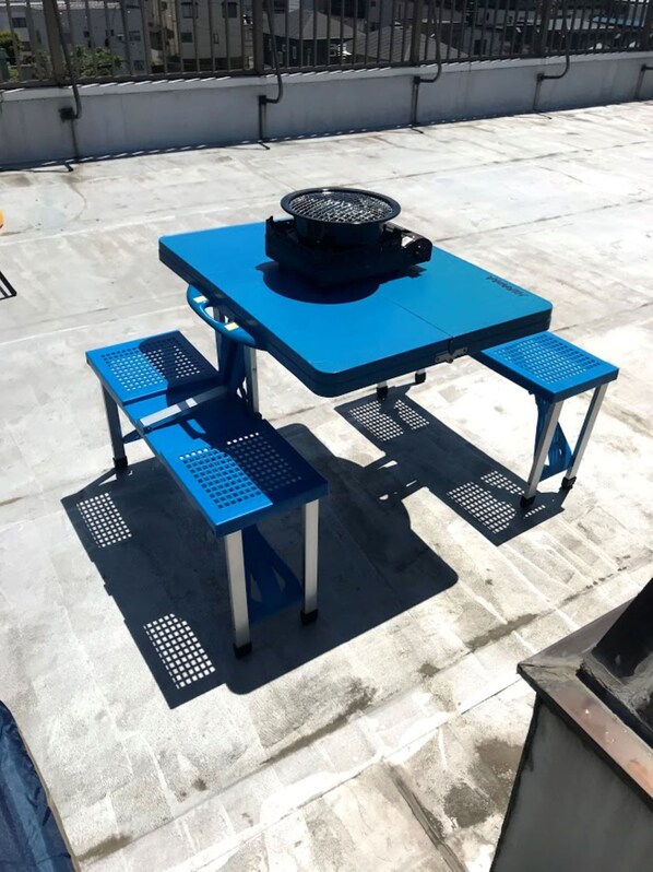 A blue outdoor table with a black grill on a rooftop patio.