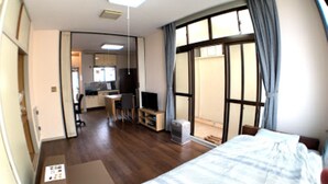 A bedroom with a bed, a desk, and a chair. There is a window with curtains and a view of the outside. - Big Stone Tsukuda 202 (Aomori)