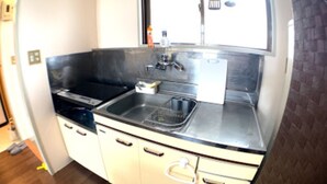 A compact kitchen with a stainless steel sink, a stove, and white cabinets. - Big Stone Tsukuda 303 (Aomori)