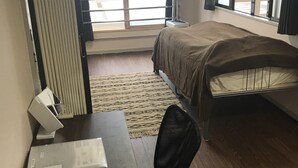 A hotel room with a bed, a desk with a chair, a window with curtains, and a radiator. - Big Stone Tsukuda 303 (Aomori)
