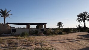 A rustic building with a wooden pergola, surrounded by dry grass and palm trees. - Bella Djerba (Sidi Salem)
