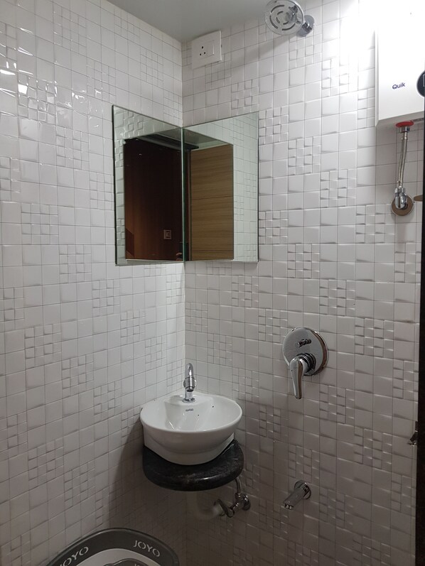 A bathroom with white tiled walls, a sink with a mirror above it, and a showerhead.