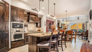 A kitchen with dark wood cabinets, stainless steel appliances, a central island with bar stools, and pendant lighting. - 4098 Coral Ridge, The 19th Hole in Coral Ridge, near golf course, firepit, heated pool, SLP 12 (Washington)