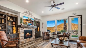 A living room with a fireplace, leather furniture, a TV, and a view of a desert landscape. - 4098 Coral Ridge, The 19th Hole in Coral Ridge, near golf course, firepit, heated pool, SLP 12 (Washington)