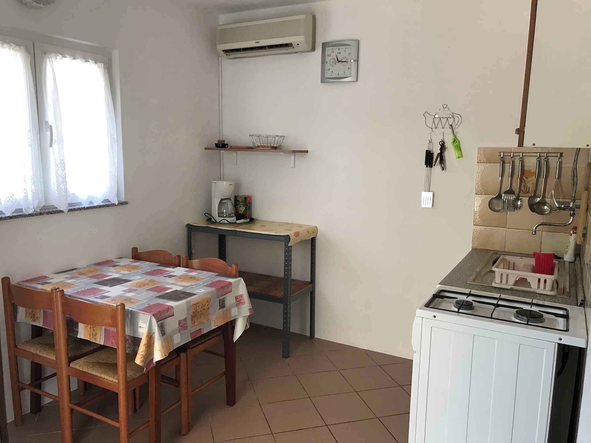 Een compacte keuken met een tafel, stoelen, een koffiezetapparaat, een klok en een gasfornuis.