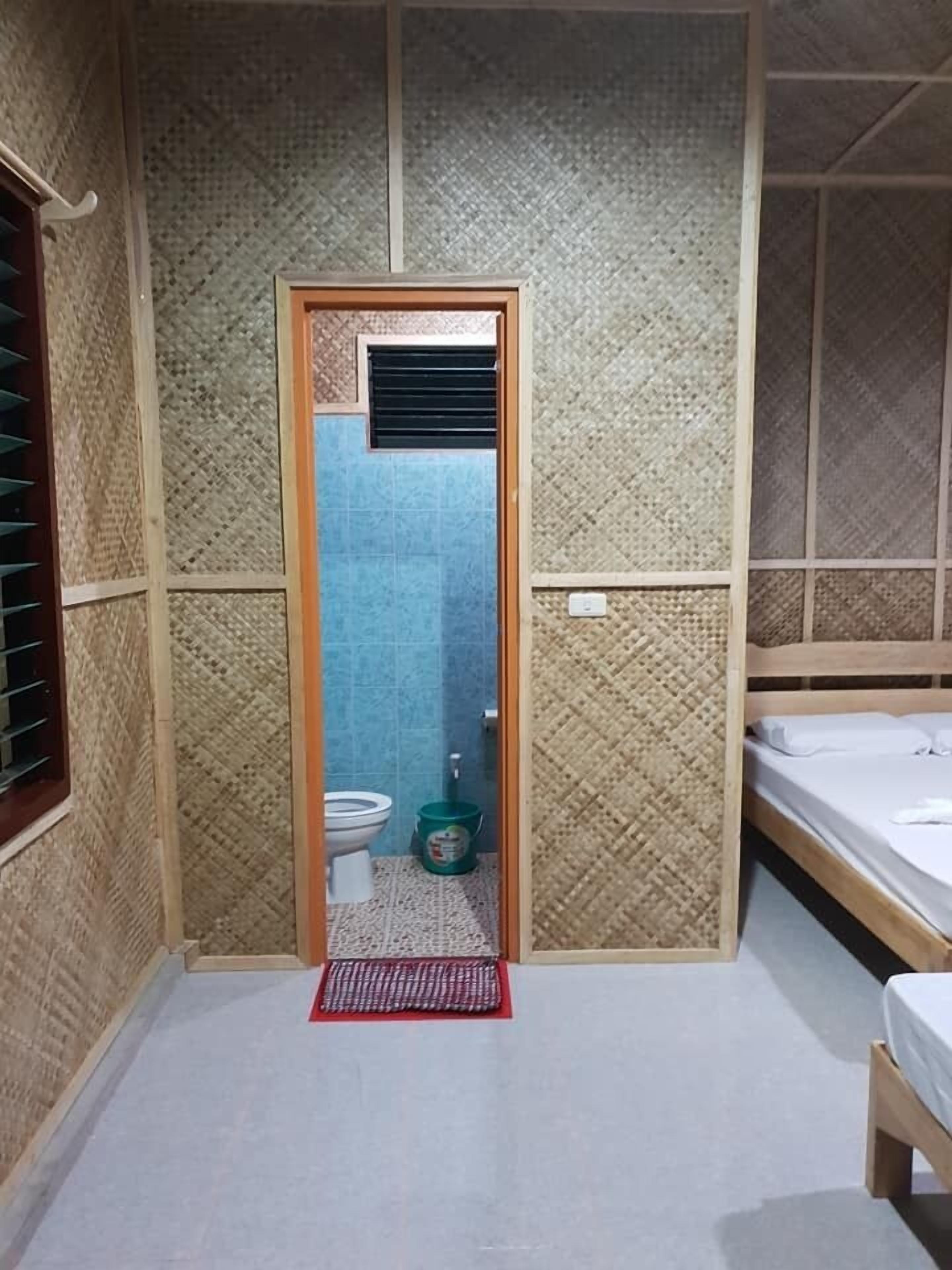 A room with a wooden door leading to a bathroom, a bed, and a small window with blinds.