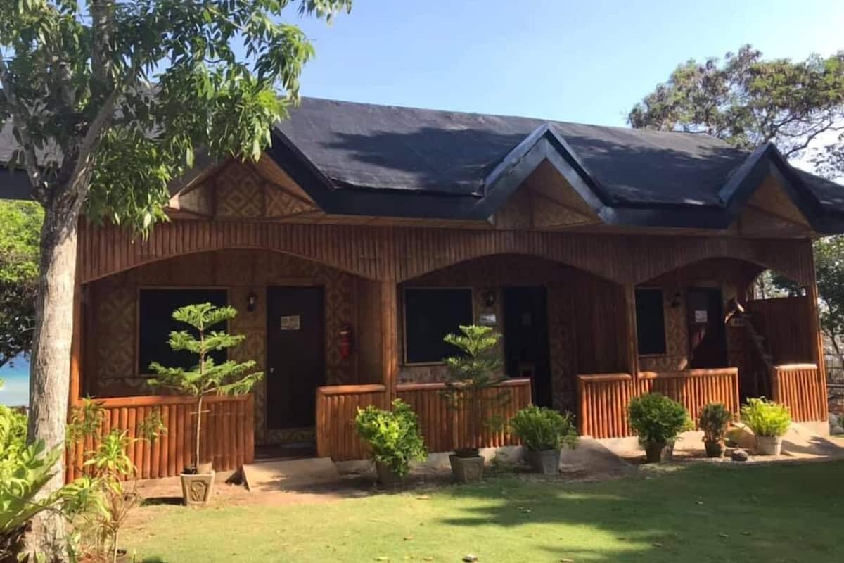 A wooden building with a gabled roof, multiple doors, and a fenced porch area with potted plants.