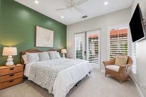 A bedroom with a bed, bedside lamps, a wicker nightstand, a chair, and a wall-mounted TV.