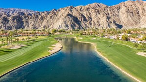 Campo de golf con un lago, rodeado de montañas y zonas residenciales.