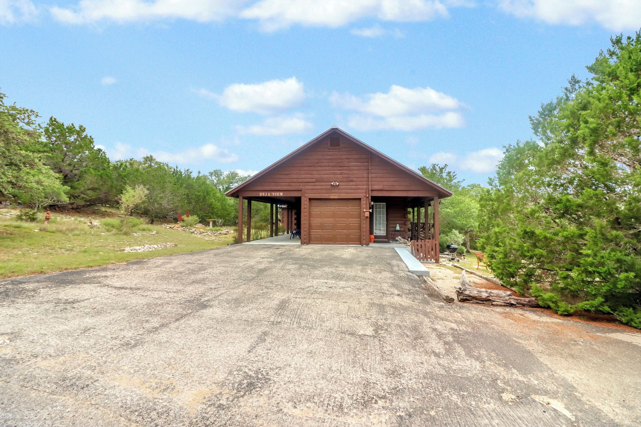 A wooden structure with a garage door, surrounded by trees and a gravel driveway.