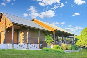 A log cabin with a porch, a small garden, and a clear blue sky.