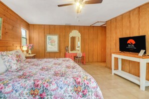 A bedroom with a bed, a desk, a television, and a ceiling fan.