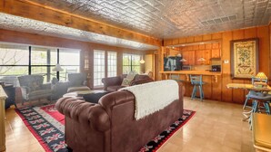 A cozy living room with a brown leather sofa, a dining area with a small table and chairs, and a kitchen area with wooden cabinets and a refrigerator. - Spacious one bedroom log cabin with views for miles! Only one mile from the Wimb (Wimberley)
