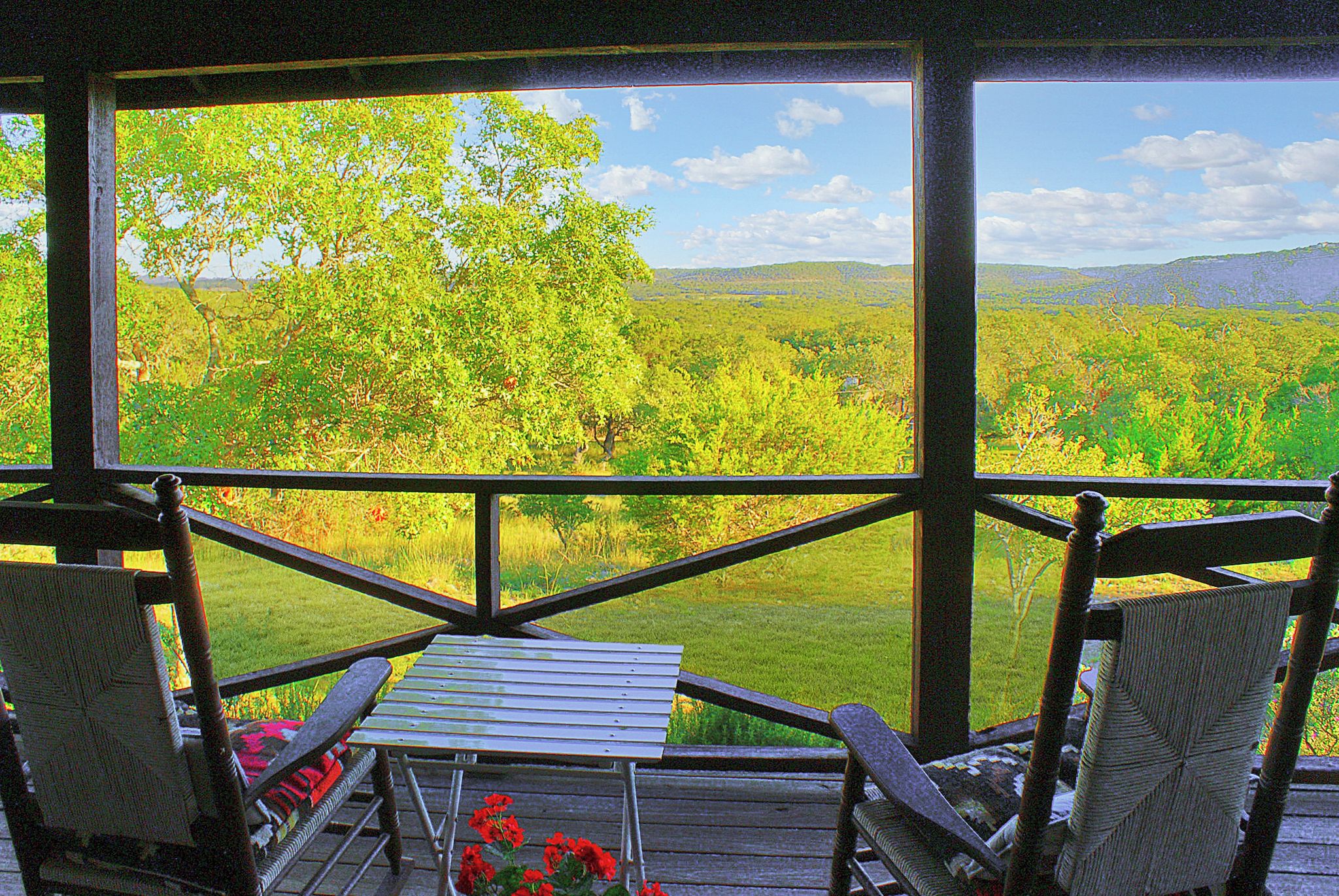 Ein überdachter Außenbereich mit Tisch und Stühlen, mit Blick auf eine üppige Landschaft mit Bäumen und Hügeln.