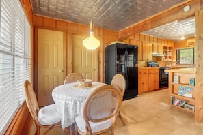 A wooden interior with a dining table, chairs, a black refrigerator, and a kitchen area.