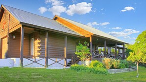 A log cabin with a porch, a small garden, and a clear blue sky. - Spacious one bedroom log cabin with views for miles! Only one mile from the Wimb (Wimberley)