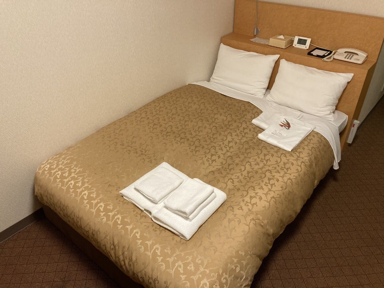 A neatly made bed with a patterned bedspread, pillows, and folded towels.
