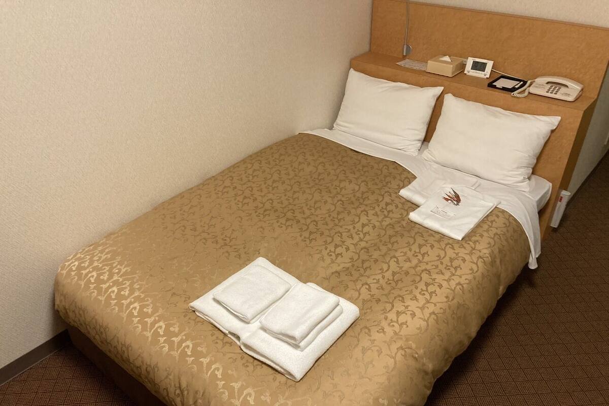 A neatly made bed with a patterned bedspread, pillows, and folded towels.