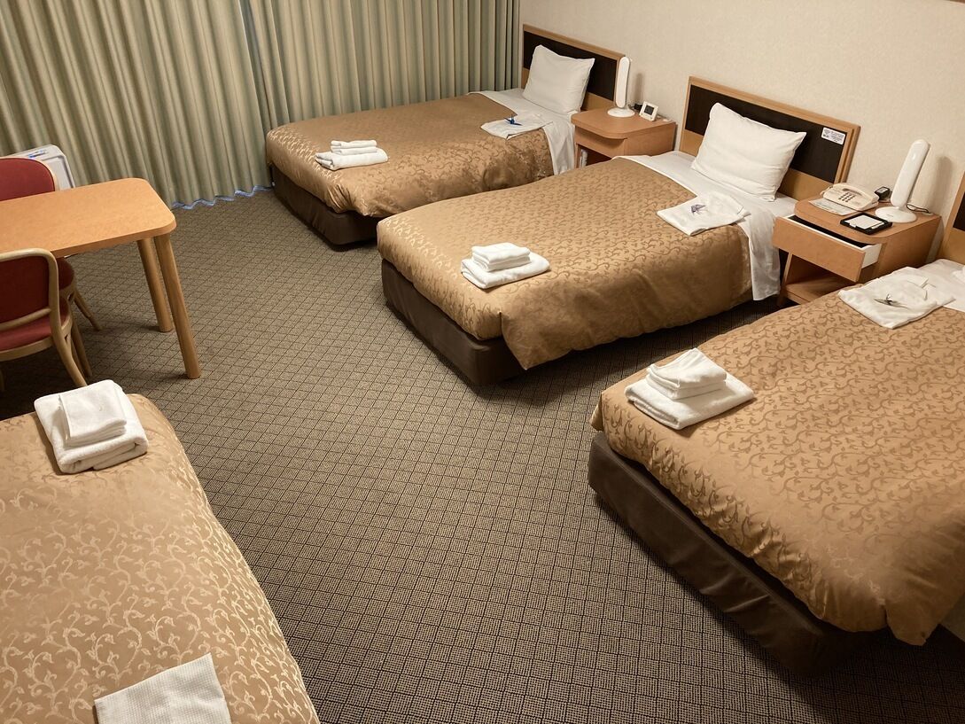 A hotel room with two beds, a desk, a chair, a nightstand, and a telephone.