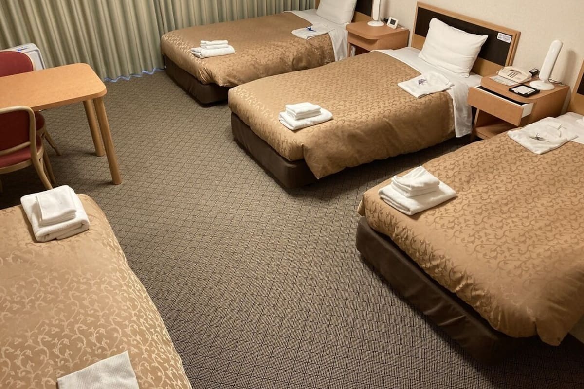 Habitación de hotel con dos camas, un escritorio, una silla, una mesita de noche y un teléfono.