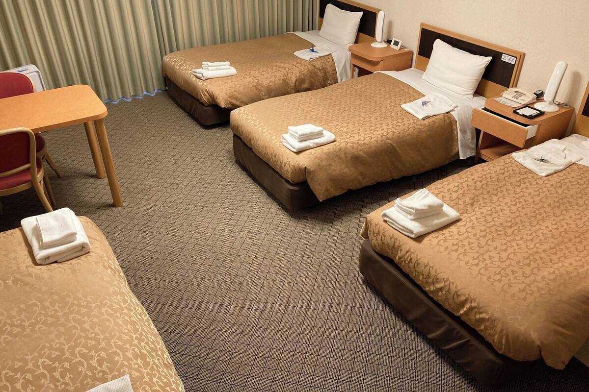 A hotel room with three beds, a desk, and a chair.