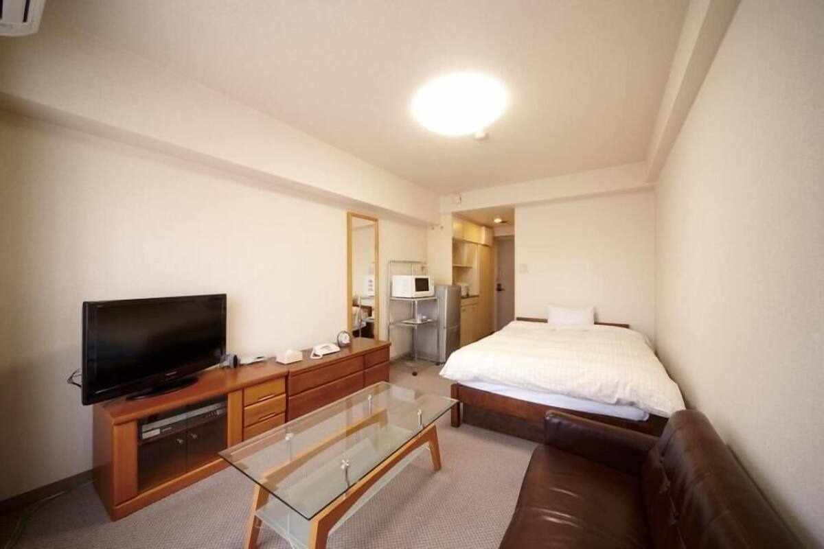 A hotel room with a bed, a television, a glass coffee table, a wooden dresser, and a microwave.