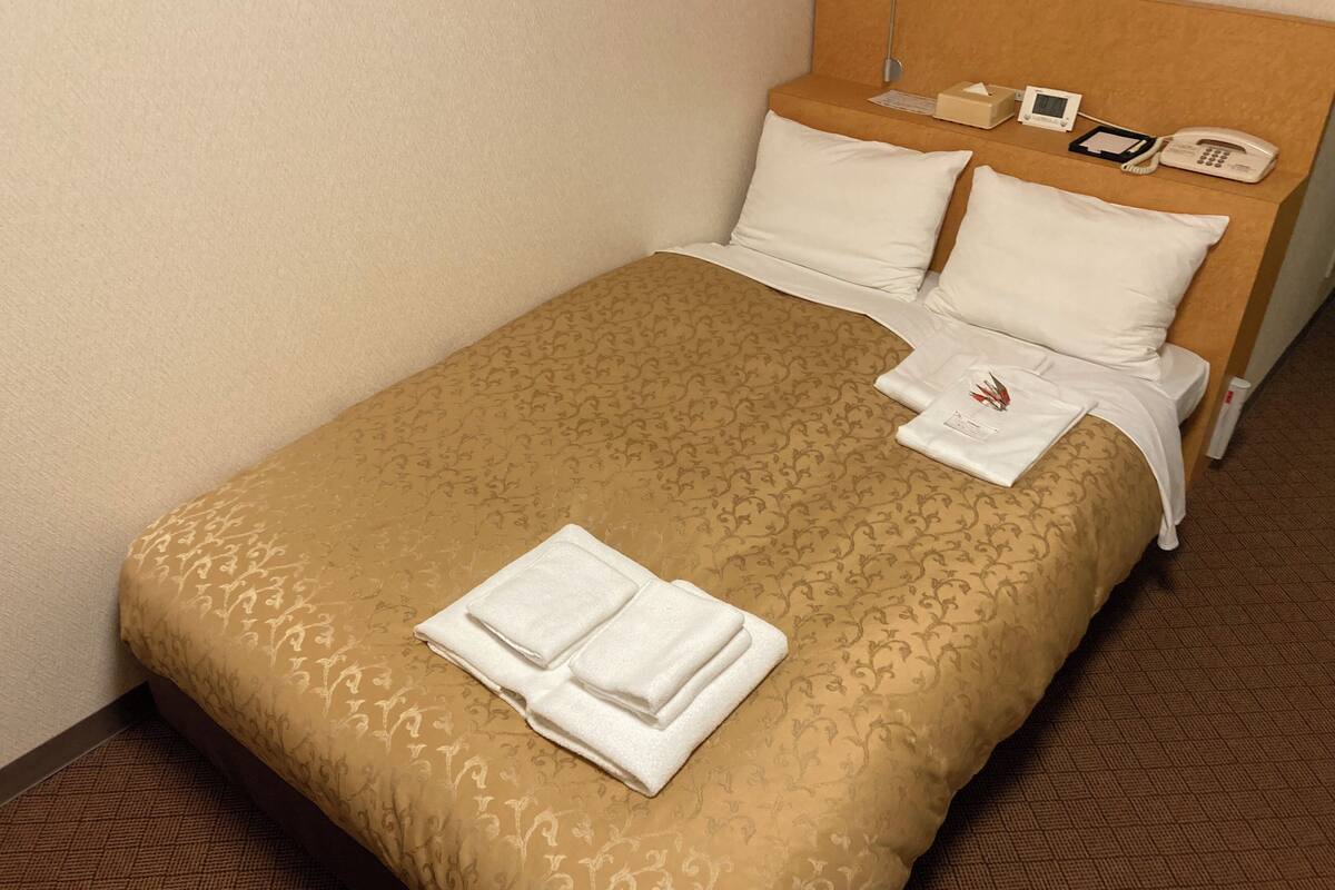 A neatly made bed with a patterned bedspread, white pillows, and folded towels.