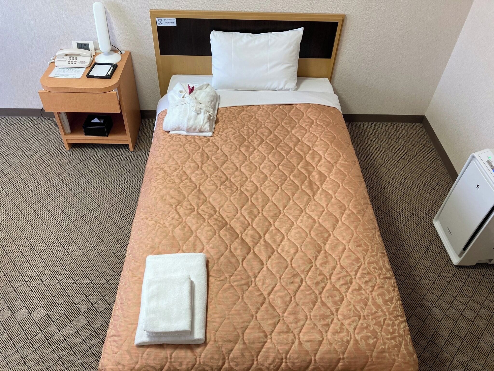 A hotel room with a bed, a bedside table with a phone and a lamp, and a small cabinet.