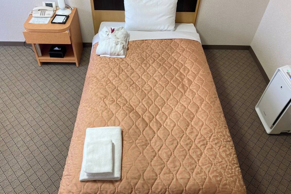 A hotel room with a bed, a bedside table with a phone and a lamp, and a small cabinet.