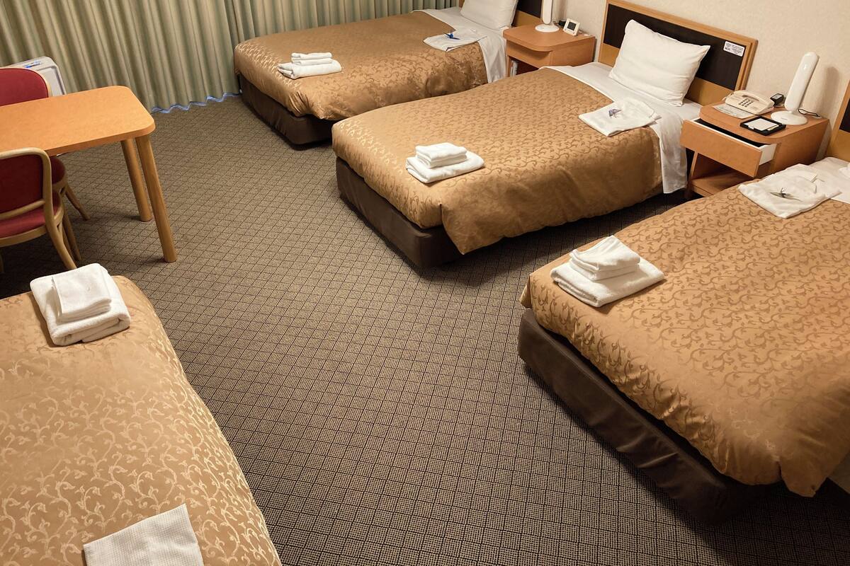 A hotel room with three beds, a desk, and a chair.