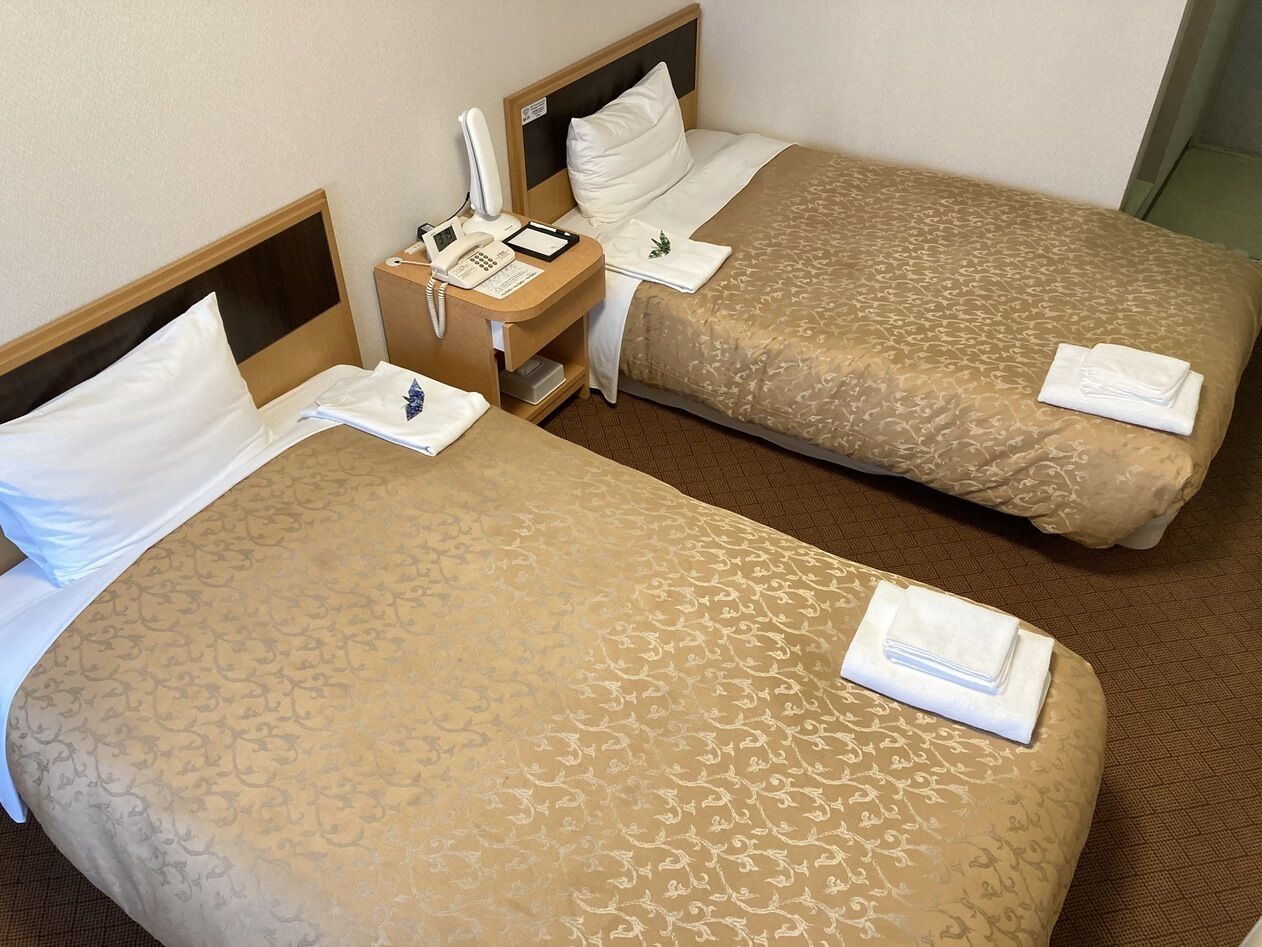 Two single beds with headboards, a bedside table with a phone and notepad, and a small nightstand with a lamp.