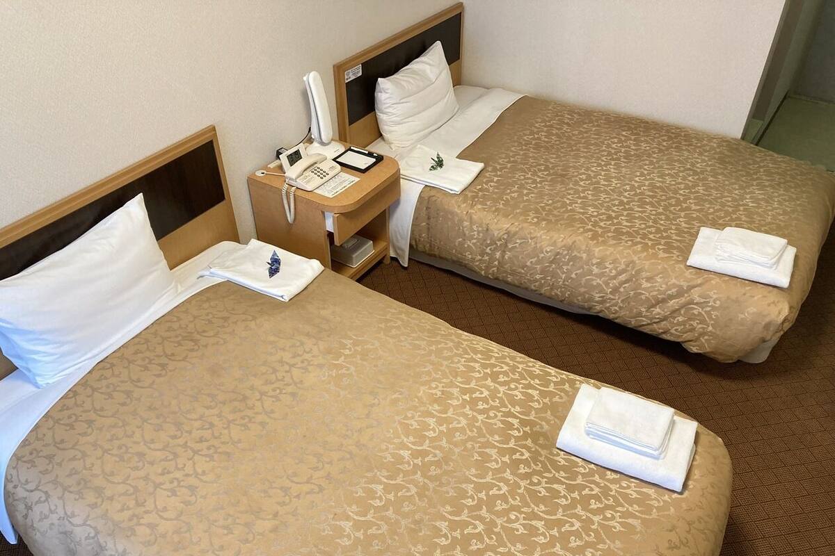 Two single beds with headboards, a bedside table with a phone and notepad, and a small nightstand with a lamp.