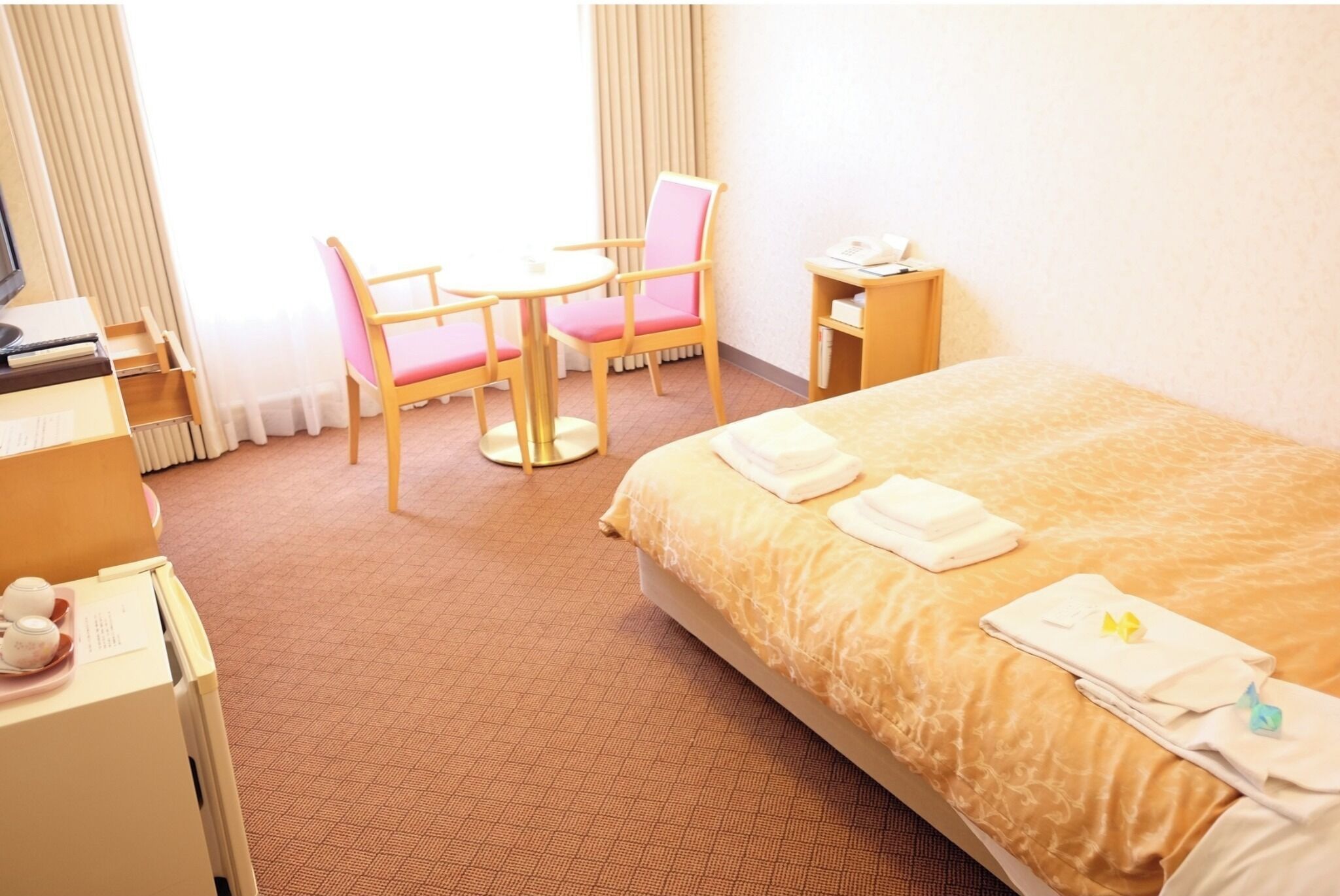 A hotel room with a bed, a desk, a chair, and a small table.