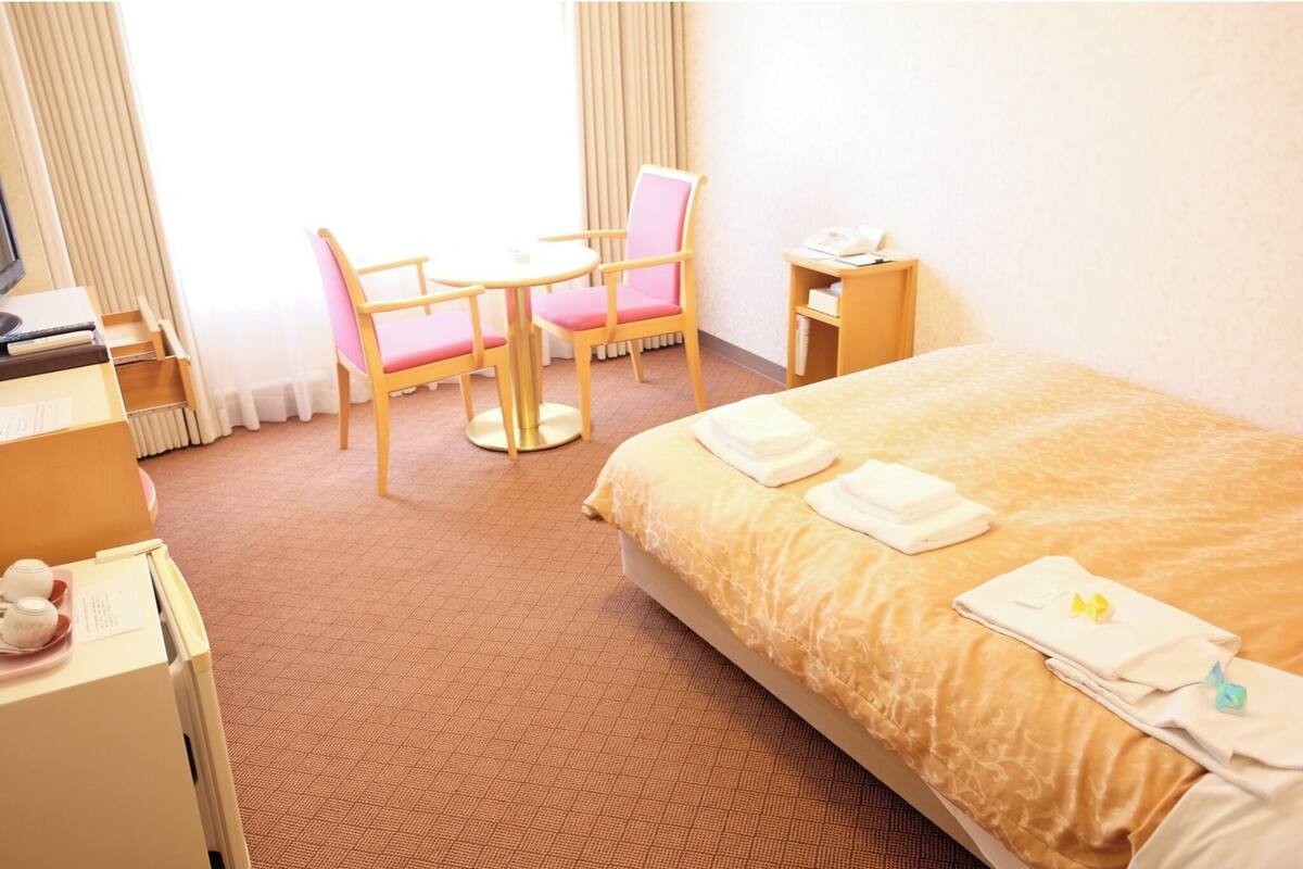 A hotel room with a bed, a desk, a chair, and a small table.