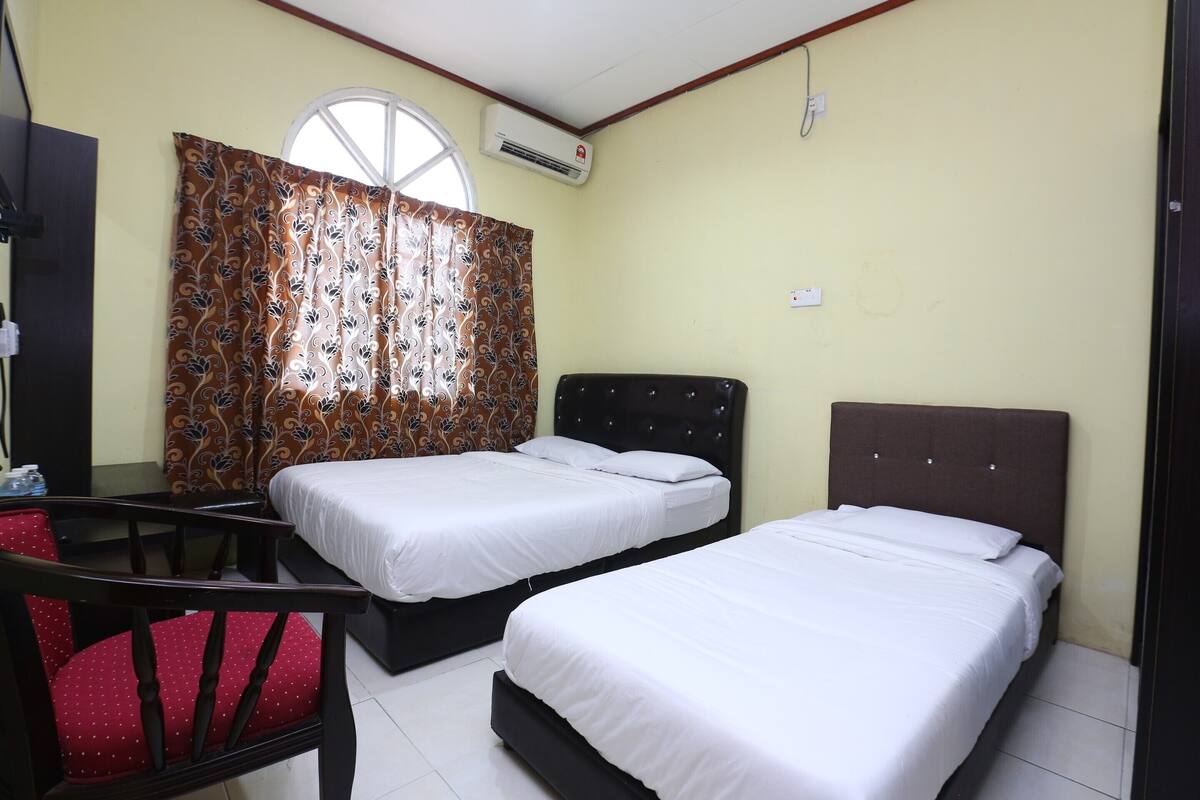 Une chambre d’hôtel avec deux lits, un bureau, une chaise et une fenêtre avec des rideaux à motifs.